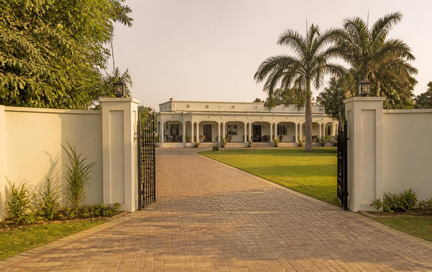 An elegant gated farmhouse estate with palm-lined driveway and lawn